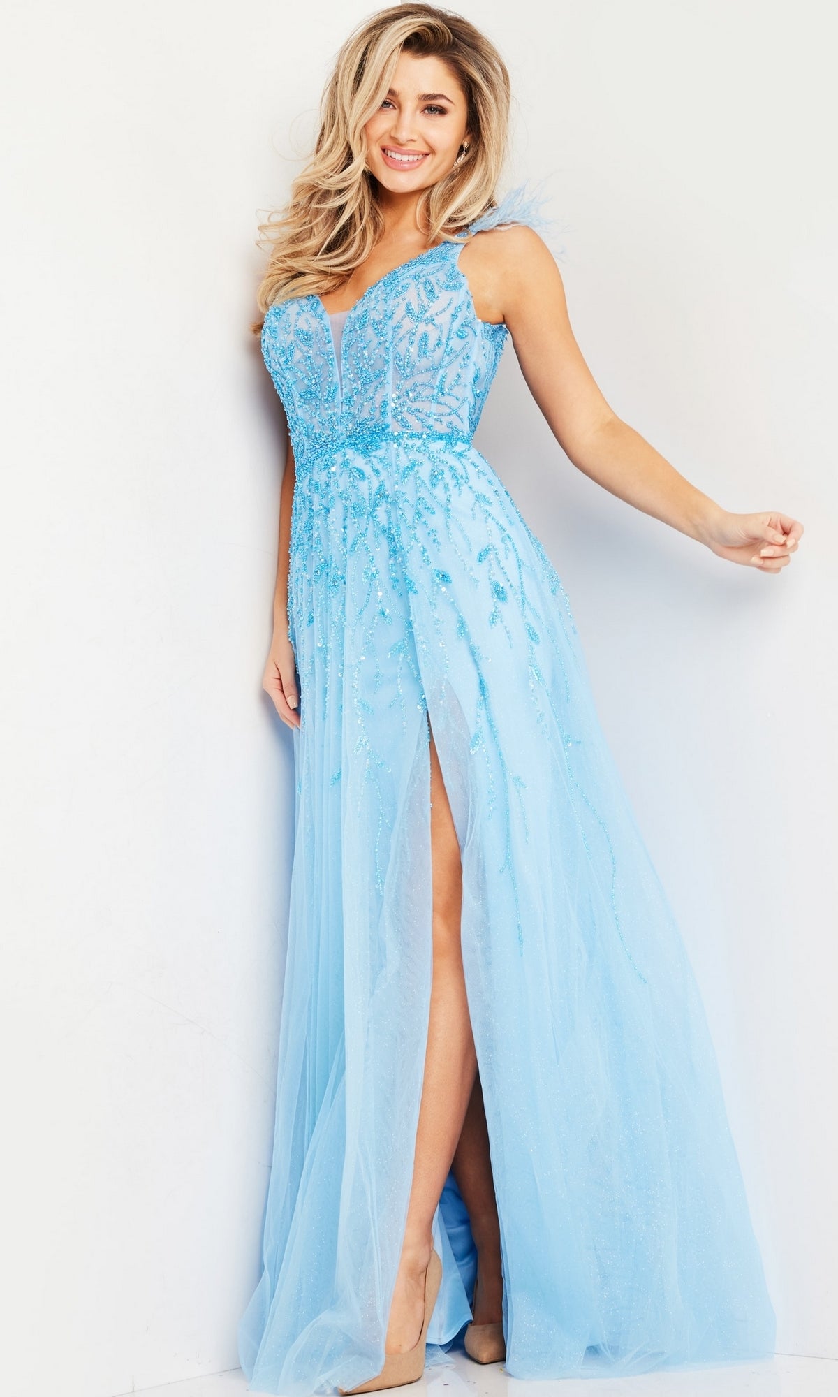 A woman smiles and poses against a white background wearing the Long Prom Dress 38430 by Jovani, featuring light blue color, a floor-length A-line silhouette, sheer overlay, v-neckline, and high slit.